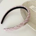 Nahaufnahme von rosa Tweed-Haarreif mit goldenem Metallemblem auf Keramikteller - Rosa