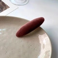 Detail view of a burgundy velvet duckbill clip on a ceramic plate with soft lighting - Pink