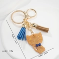 Charmante amberkleurige acryl katten sleutelhanger met blauwe strik en kwastjes - Amberkleurige Kat Stijl (1)