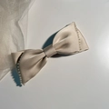 Macro detail of champagne satin bow hair clip with pearl embellishments on edges - Beige