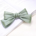 Elegant sage green satin double bow hair clip placed on an open book background - Green