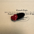 Close-up of a glossy red heart hair clip on a black oval base and textured beige fabric - Red Heart Style