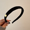 Detailed view of a thick black plush headband featuring a small round gold metal accent - Black