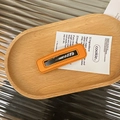 Detail shot of a square orange leather hair clip with fine stitching on a wooden tray - Orange