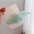 Detailopname van een mintgroene geborduurde blad-haarklem op een witte presentatiekaart - Groen