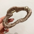 Détail d'une pince à cheveux en satin champagne avec grande perle et décor de feuille en métal - Marron