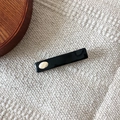 Minimalist black rectangle hair clip with gold logo label on knit fabric background - Black