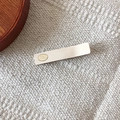 Minimalist matte cream hair clip with oval gold logo tag on soft knit background - White