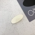 Détail d'une pince à cheveux ovale jaune crème sur un fond texturé en pierre minimaliste - Blanc