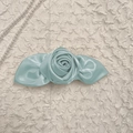 Detail van een lichtblauwe satijnen roos haarclip op een elegante witte getextureerde stof - Blauw