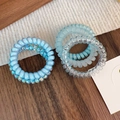 Detailed view of various blue spiral telephone wire hair coils on a textured wooden background - Blue Series Spiral Hair Rings