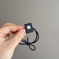 Detail of black elastic hair tie with square smile charm and golden metal ends - Black (D-5855-4)