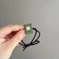 Close-up of olive green square bead with smile engraving on black elastic hair tie - Grass Green (D-5855-3)