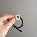 Detail view of a black elastic hair tie with a beige rectangle smiley face charm - Off-white (D-5855-1)