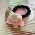Close-up of black elastic hair tie with large faux pearl and golden metal accents - White