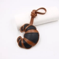 Detail view of croissant-shaped leather bag charm with brown contrast stitching and lanyard - Black Coffee