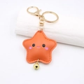 Detail view of orange leather star keychain with cute smiley face and golden bell accent - Lobster Clasp Style / Orange