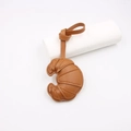 Close-up of brown leather croissant bag charm with detailed stitching and a hanging strap - Light Coffee