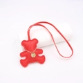 Macro detail of red faux leather bear bag charm with gold chain and rhinestone tag - Red