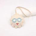 Dettaglio del ciondolo a sole in pelle color crema con occhiali blu e sorriso rosso - Beige