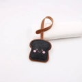 Close-up of black leather toast charm with cute face and brown stitched strap - Black