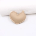 Dettaglio di ciondolo a cuore in pelle color crema con trama a grana e cuciture - Cachi
