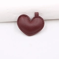 Dettaglio di ciondolo a cuore in pelle bordeaux con trama litchi e cuciture rifinite - Borgogna