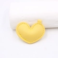 Dettaglio di un ciondolo a cuore in pelle gialla con cuciture precise e anello superiore - Giallo