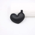 Dettaglio di un ciondolo a cuore in pelle nera con trama a grana e cuciture su sfondo bianco - Nero