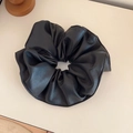 Close-up of black faux leather scrunchie with rich texture and subtle glossy finish - Black