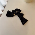 Détail du chouchou nœud en velours noir avec un médaillon doré sur une surface beige - Pendentif Métallique Nœud Velours Noir Scrunchie (A-3289-1)