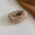 Detail eines Winter-Haargummis aus Plüsch mit bunten Punkten auf beigem Mohair - Braun