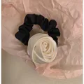 Detail eines cremefarbenen Satin-Rosen-Haargummis mit schwarzem Faltenband auf Papier - Creme Rose