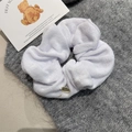 Macro shot of white towel fabric scrunchie with a round gold metal charm detail - White Scrunchie