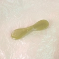 Detailed close-up of light green jade gua sha massager on soft pink wrinkled paper - Green