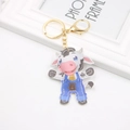 Cartoon cow leather keychain with gold metal clasp and blue overalls on white background - Cow