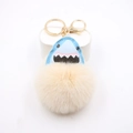 Détail du porte-clés pompon abricot en peluche avec motif requin en cuir et clip doré - Blanc Cassé