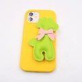 Detailed close-up of yellow phone case with green 3D giraffe pendant and pink bow - Grass Green