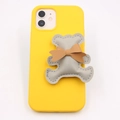 Yellow phone case featuring a gray leather bear charm and brown bow tie accessory - Gray