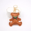 Detailed close-up of brown leather bear keychain with red plaid bow and gold metal clasp - Bear Charm / Coffee
