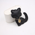 Detailed view of a black leather cat charm with a gold chain and a round metal logo tag - Black