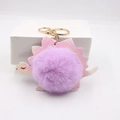 Close-up of pink dinosaur pompom keychain with gold hardware and plush texture - Taro Purple