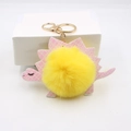 Détail du porte-clés dinosaure en cuir rose avec pompon jaune et fermoir mousqueton doré - Jaune