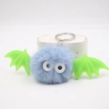 Close-up of blue plush bat keychain with green wings and metal ring on white stand - Light Blue