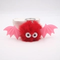 Close-up of fluffy red bat plush keychain with pink wings and large funny eyes detail - Red