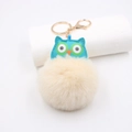 Détail du pendentif hibou en simili cuir bleu avec pompon beige et porte-clés doré - Porte-clés Doré / Blanc Cassé