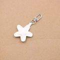 Close-up of a white star-shaped leather charm with fine stitching and silver metal hook - White