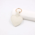 Dettaglio portachiavi a forma di cuore in pelle litchi color panna con anello dorato - Cuore Magnetico / Bianco