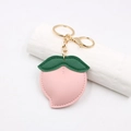 Détail du porte-clés pêche en cuir rose avec feuille verte et fermoir doré - Style Pêche / Rose