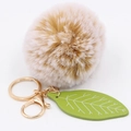 Detailed shot of beige faux rabbit fur ball keychain with green leaf and gold hardware - Mixed Khaki